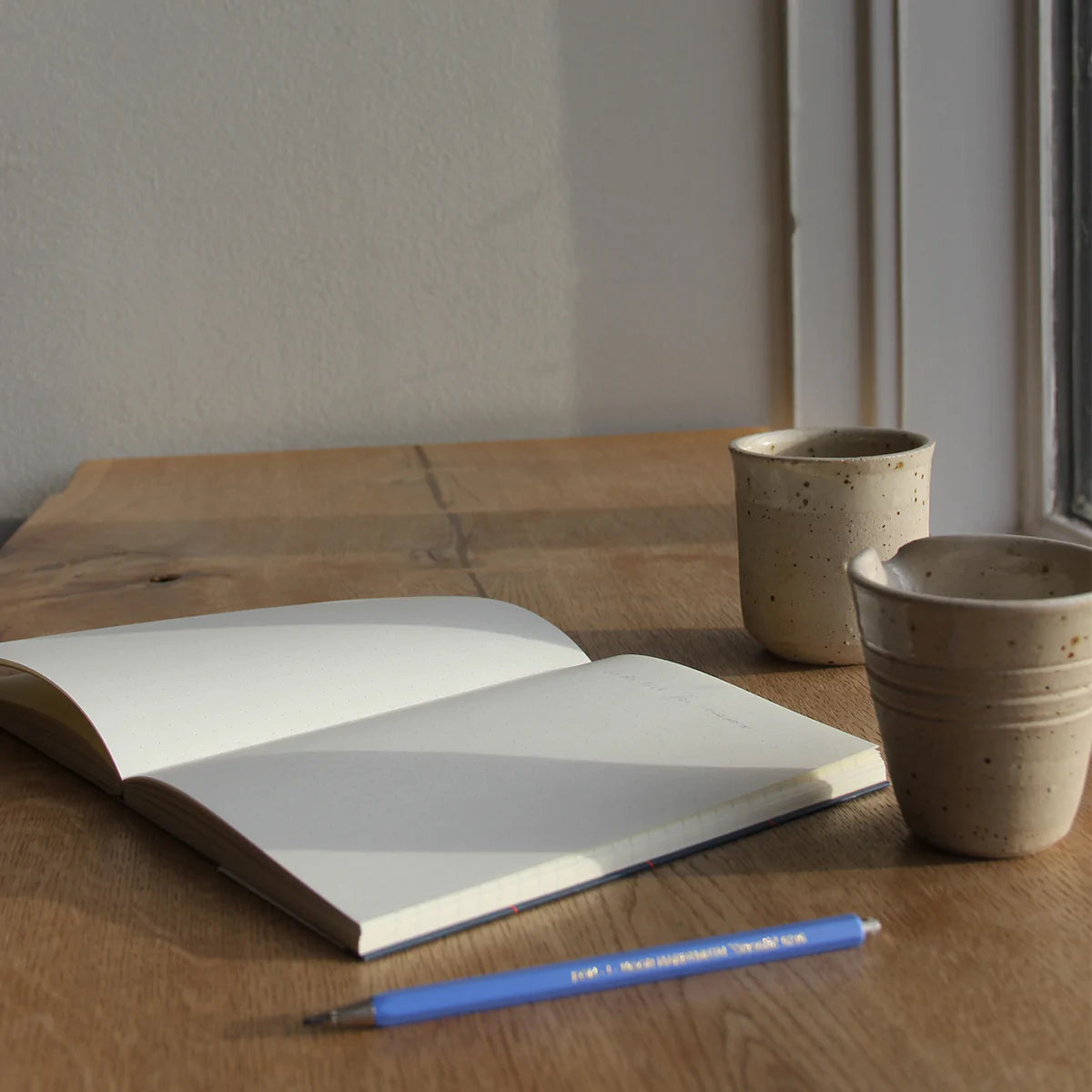 Carnet UMA rose de notem posé ouvert sur un bureau avec tasse et crayon