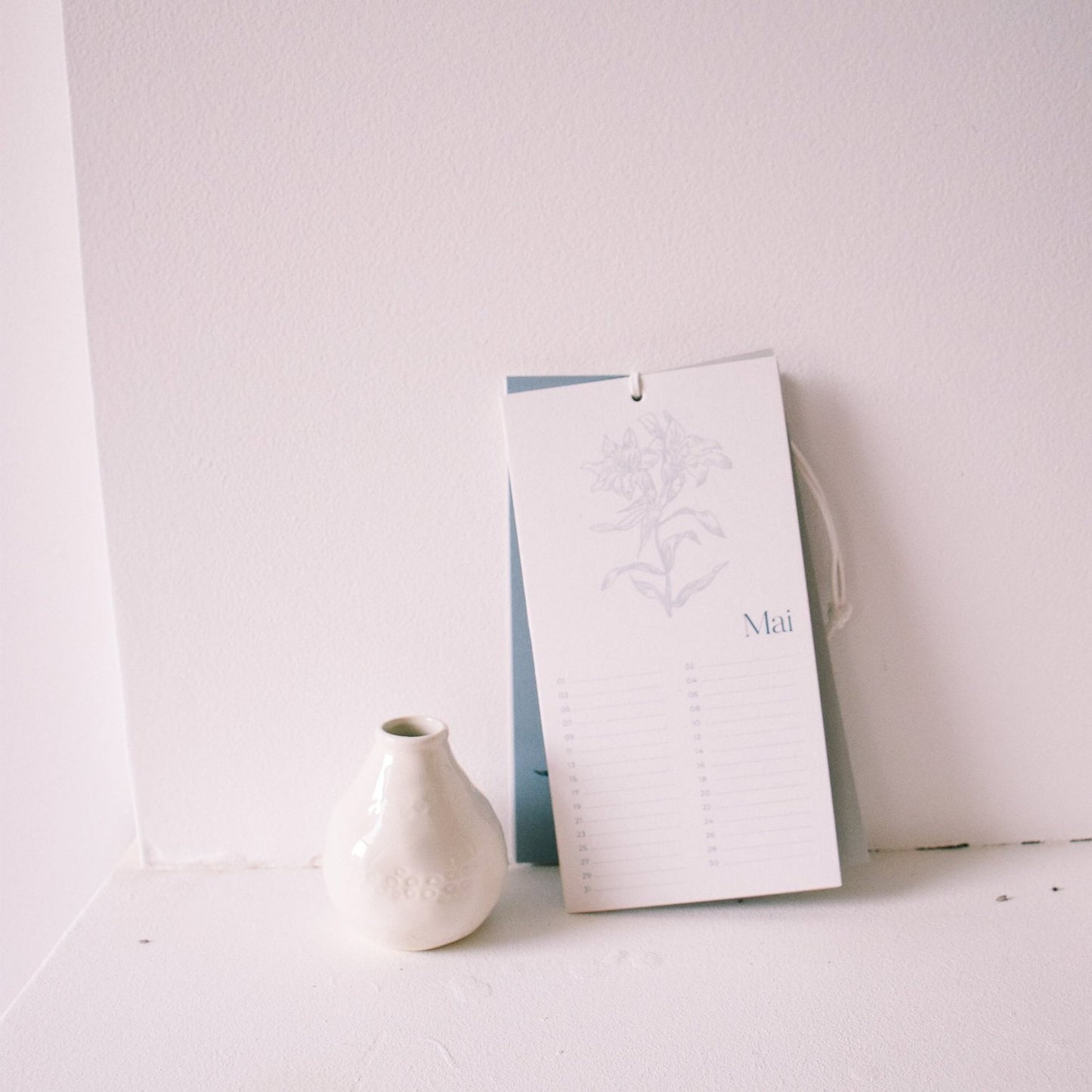 Calendrier sur mu blanc avec vase blanc