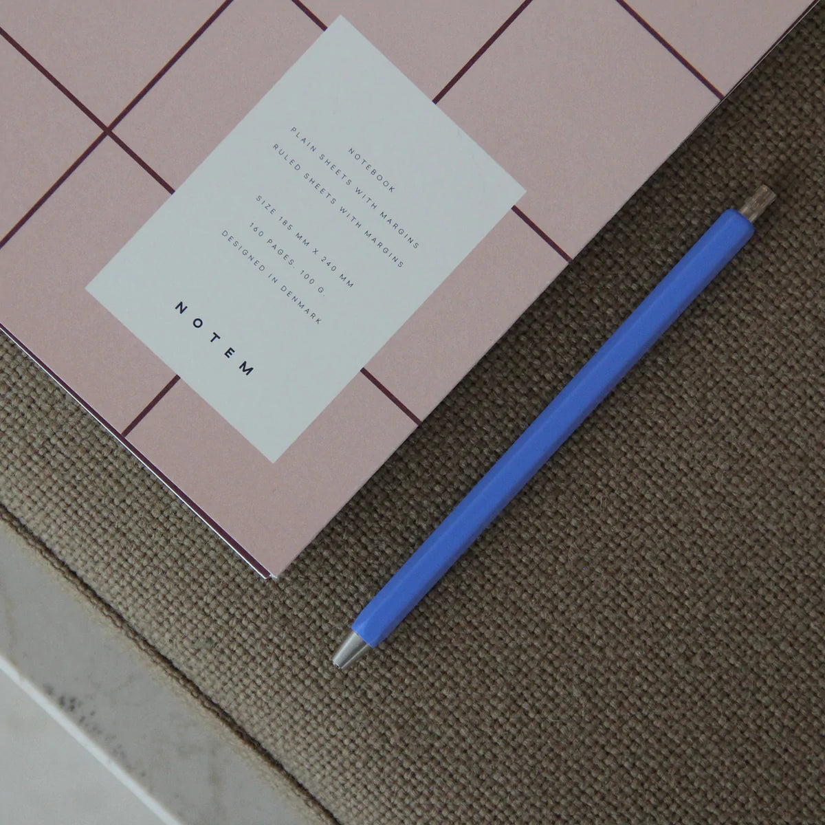 Carnet couverture rose UMA de notem sur canapé à coté d'un crayon bleu