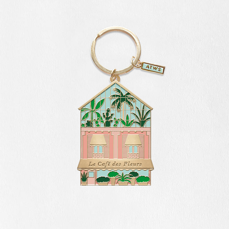 Porte clef doré all the ways to say avec bâtiment rose type café avec plantes verte et verrière 